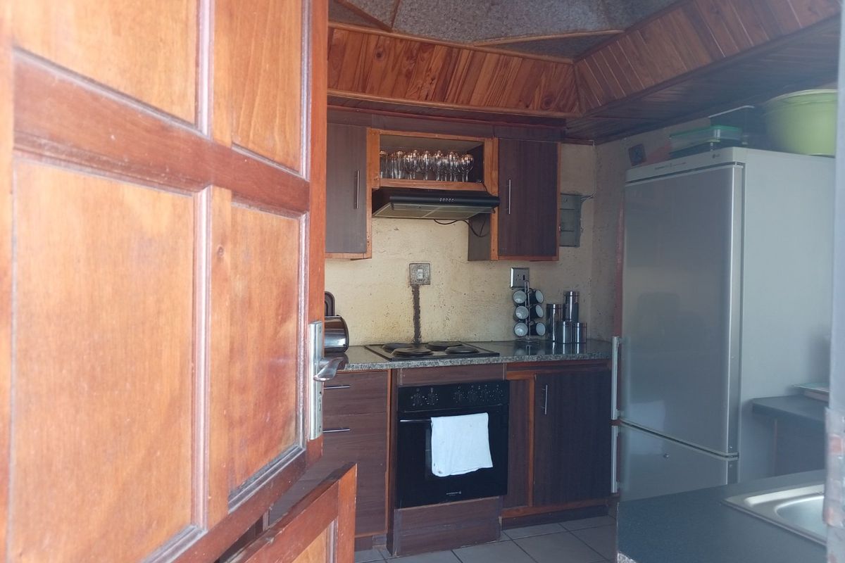 A compact kitchen featuring timber ceiling paneling, built-in cabinetry, an electric hob, and an oven, offering a functional layout with potential for modern updates.