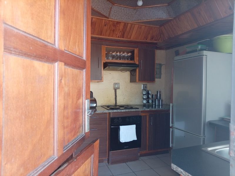 A compact kitchen featuring timber ceiling paneling, built-in cabinetry, an electric hob, and an oven, offering a functional layout with potential for modern updates.