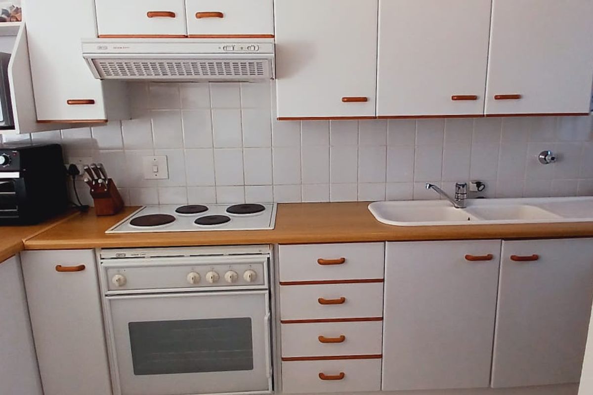 A functional kitchen featuring white cabinetry, laminate countertops, a built-in oven with electric hob, and a double basin sink with tiled backsplash.