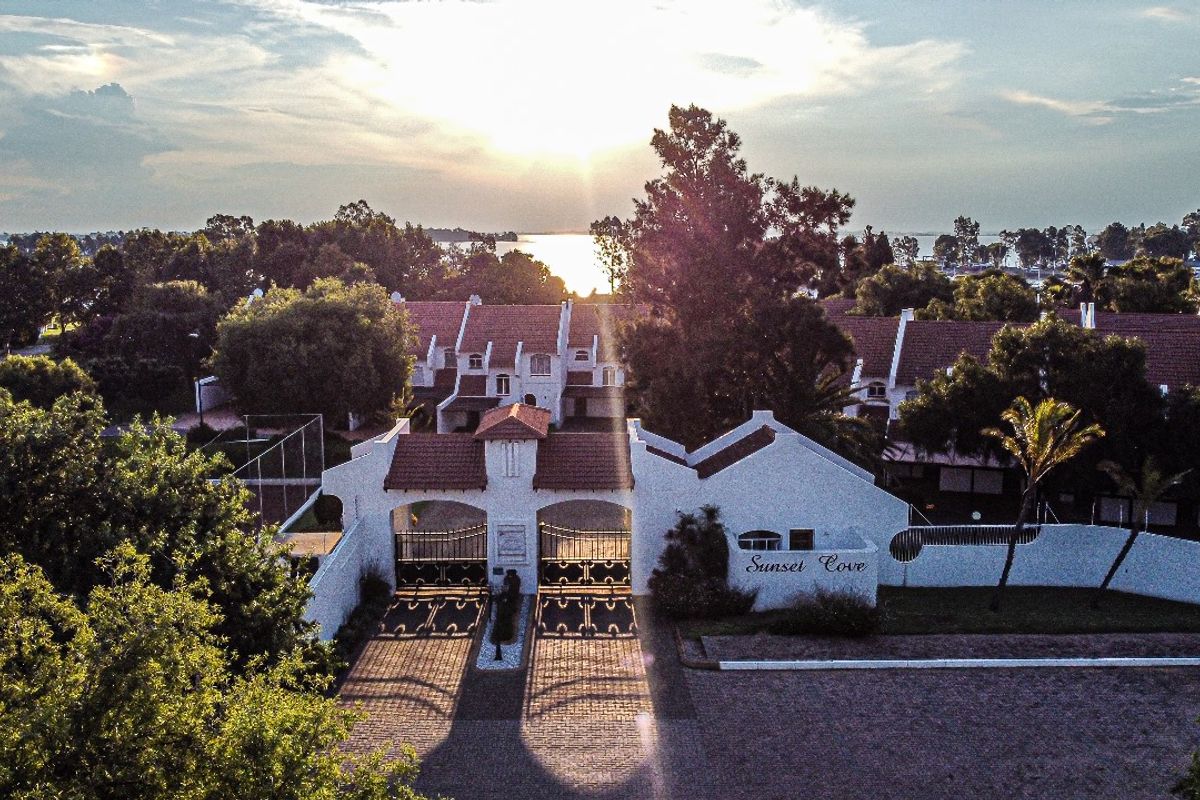 Aerial view of the Sunset Cove residential complex entrance, featuring a gated access point, paved driveway, and established landscaping at sunset.