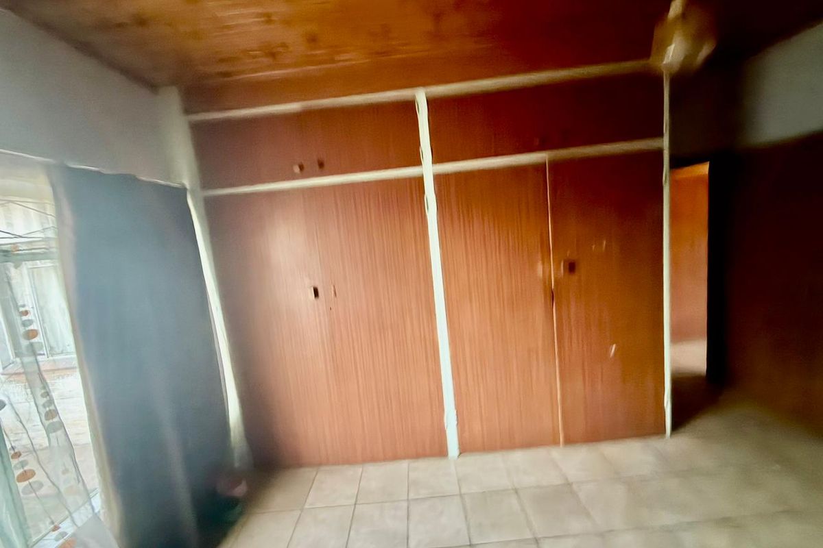 A bedroom featuring built-in wooden cabinetry, tiled flooring, and a timber-clad ceiling, offering a functional space with potential for modernization.