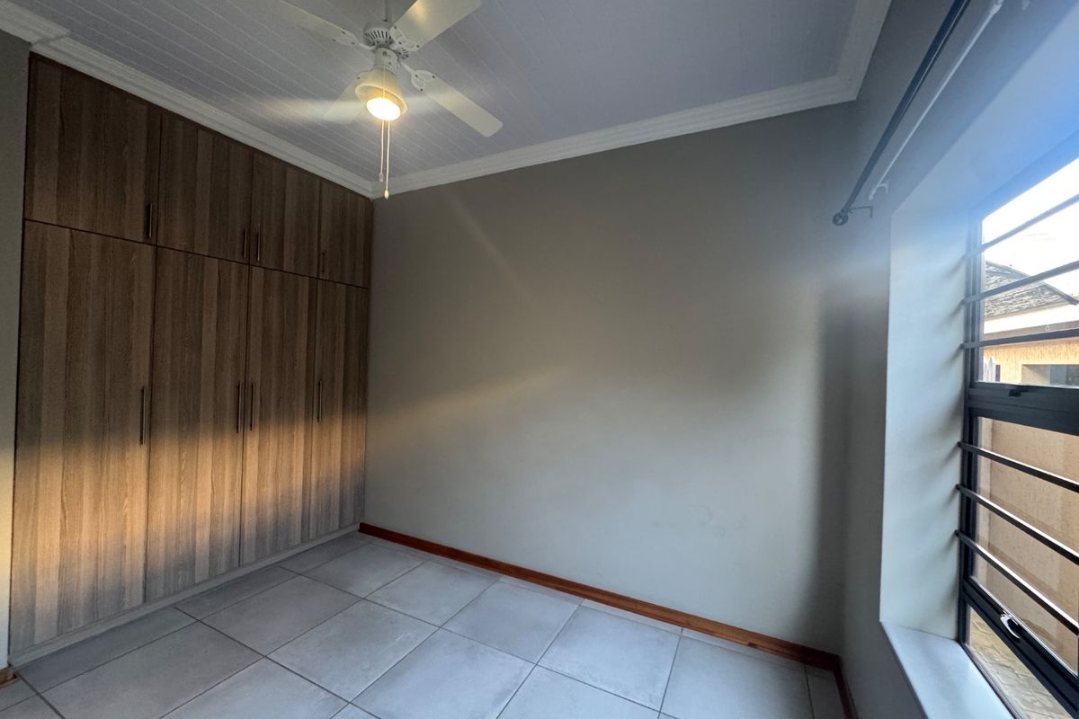 A clean, empty bedroom featuring modern wood-finish built-in cupboards, tiled flooring, and a ceiling fan, offering a neutral space ready for personalization.
