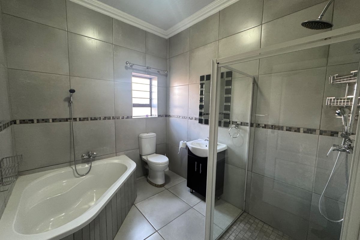 A well-maintained bathroom featuring a bathtub, separate shower enclosure, vanity basin, and toilet with neutral floor-to-ceiling wall tiles.