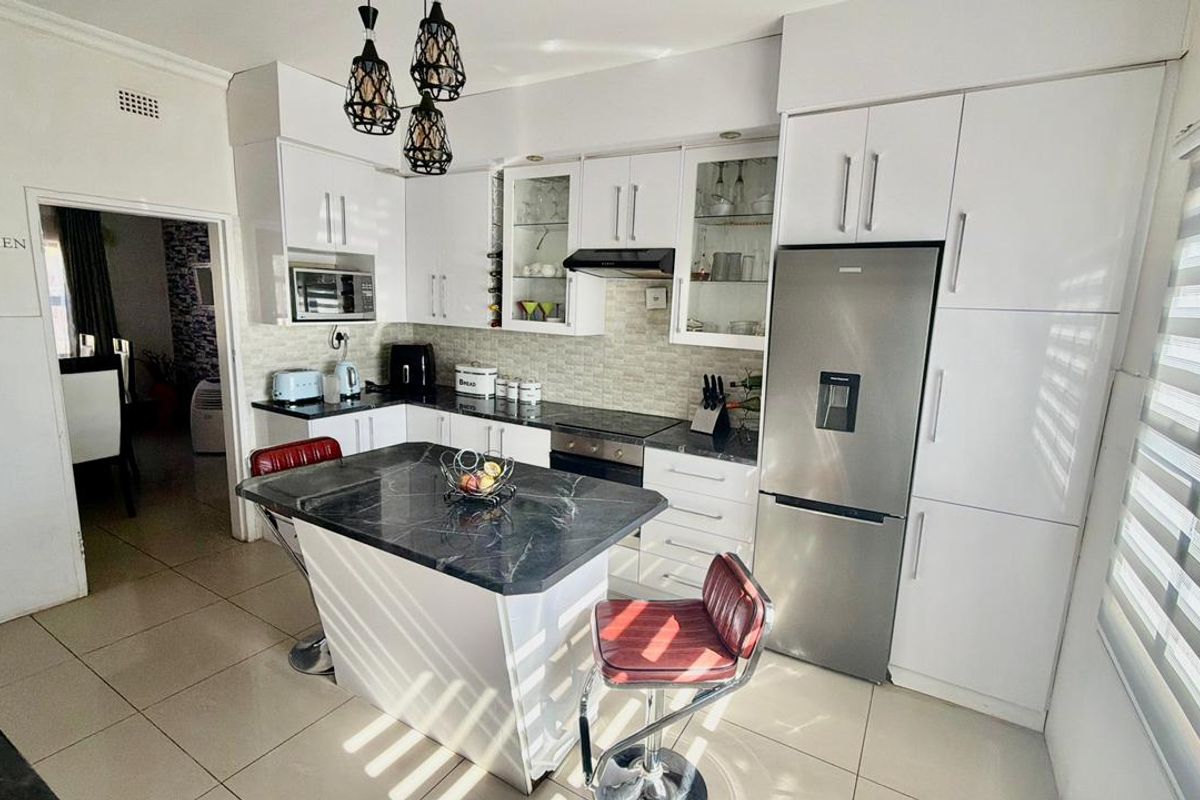 Modern kitchen featuring white cabinetry, dark stone countertops, a central island, and integrated appliances, creating a functional and bright culinary space.