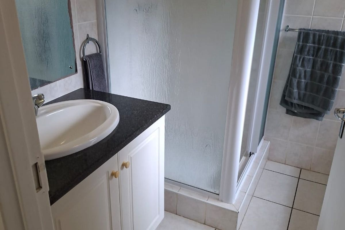 A functional bathroom featuring a vanity with a granite countertop, a drop-in basin, and a glass-enclosed shower with tiled finishes.