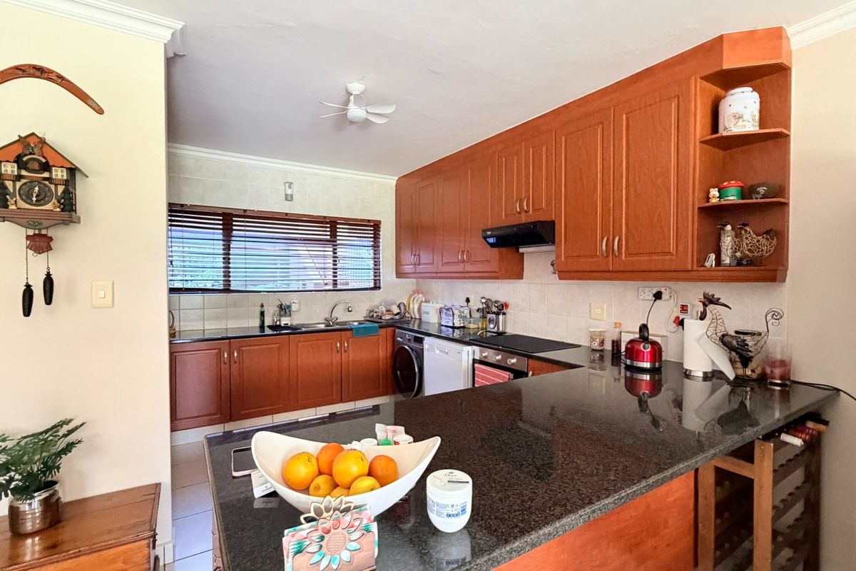 Functional kitchen featuring warm-toned wooden cabinetry, dark granite countertops, integrated appliances, and a practical breakfast bar layout.