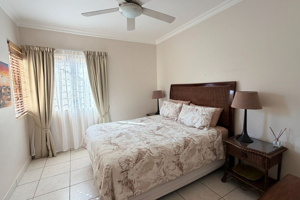 A well-lit bedroom featuring neutral tiled flooring, a ceiling fan, and classic cornice detailing, providing a comfortable and functional living space.