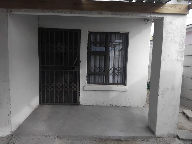 A covered entrance patio featuring a concrete floor, security gate, and window security bars, showing signs of wear and requiring maintenance.