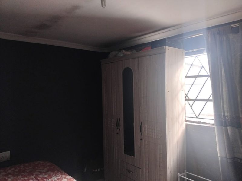A bedroom featuring security bars on the window and visible ceiling water staining, requiring maintenance and cosmetic updates.