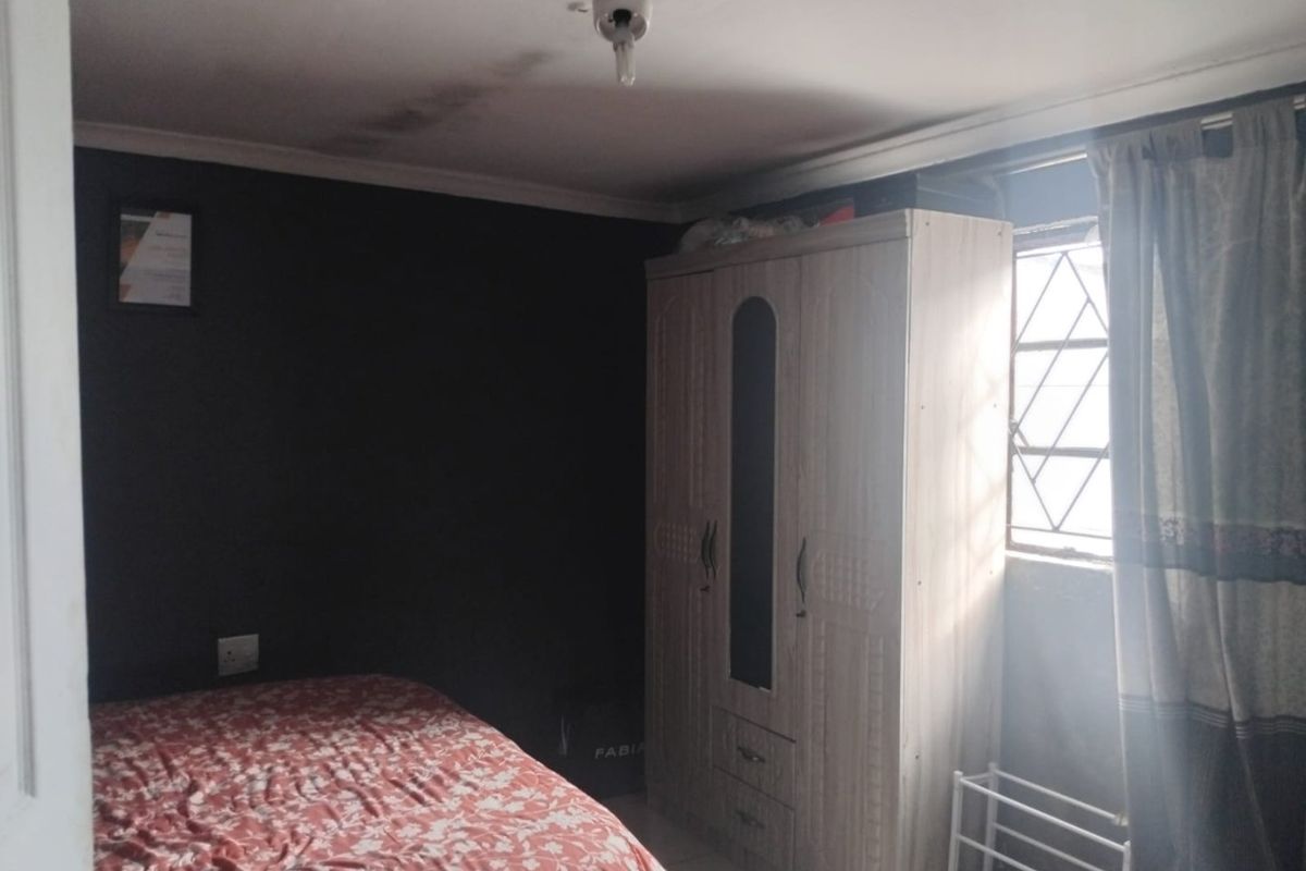 A bedroom featuring dark painted walls, a window with security bars, and visible ceiling water staining.