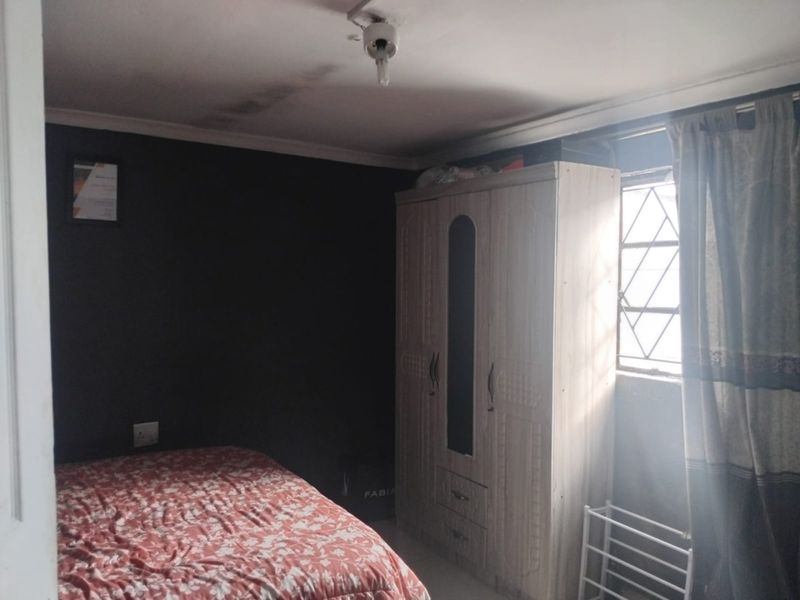 A bedroom featuring dark painted walls, a window with security bars, and visible ceiling water staining.