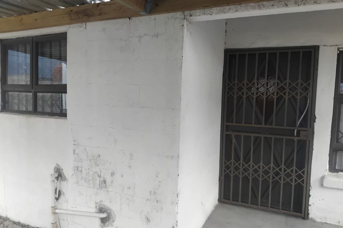 Rear exterior view showing a covered patio area with security gate, aluminium windows, and visible wear to the masonry walls.