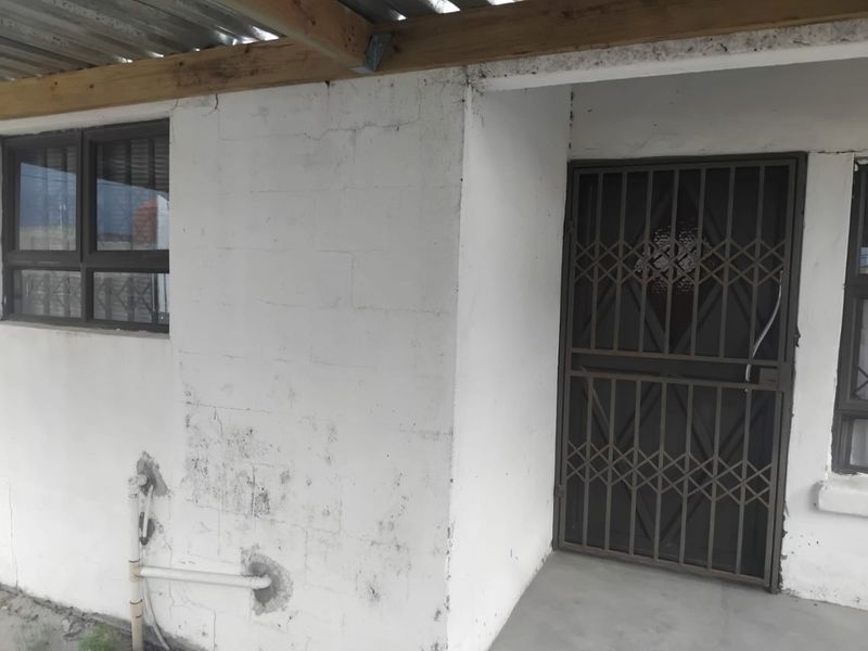 Rear exterior view showing a covered patio area with security gate, aluminium windows, and visible wear to the masonry walls.