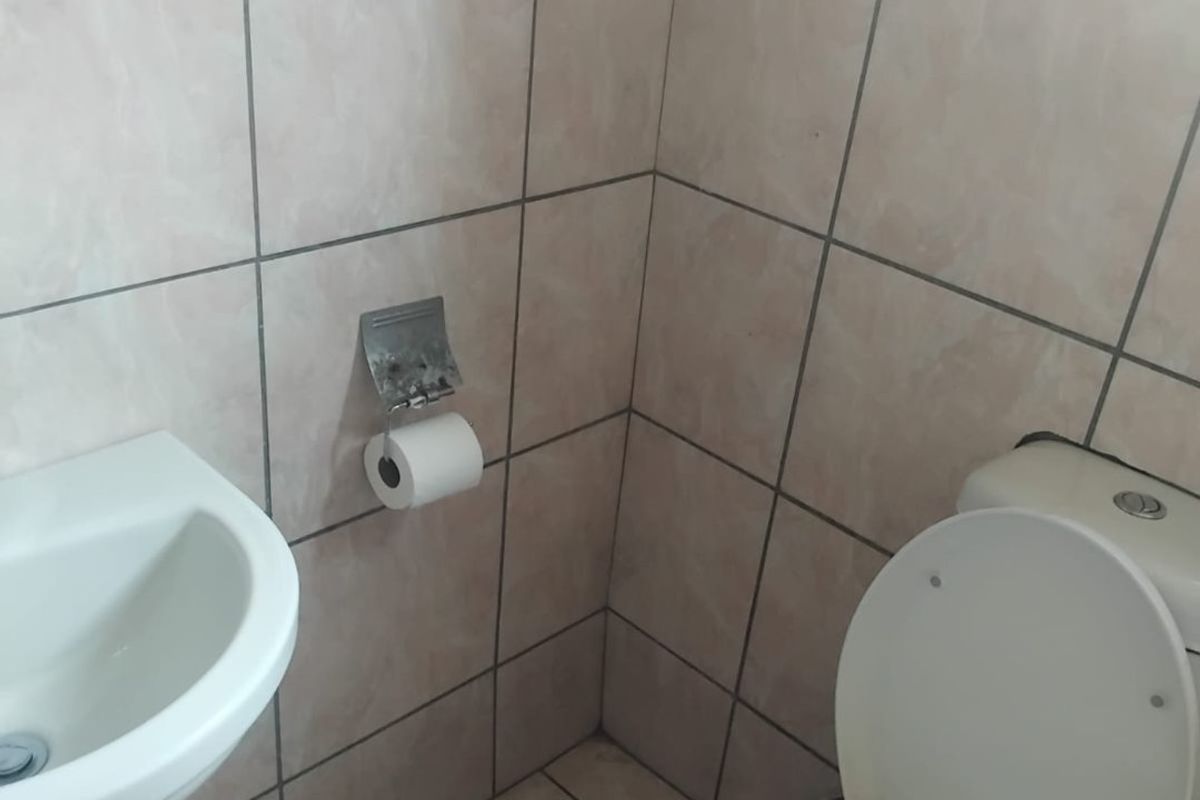 A compact bathroom featuring a pedestal basin and toilet with neutral ceramic wall and floor tiling.