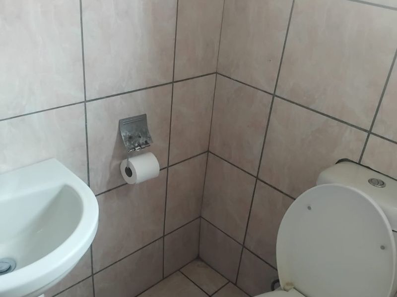 A compact bathroom featuring a pedestal basin and toilet with neutral ceramic wall and floor tiling.