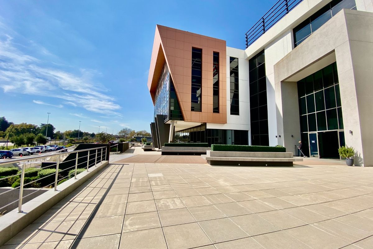Modern commercial building exterior featuring a spacious paved terrace, contemporary metal and glass facade, and integrated concrete seating areas.