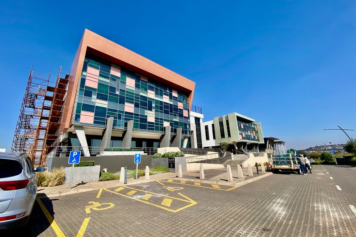 Modern commercial office building exterior featuring a glass facade, paved parking area, and ongoing maintenance scaffolding.