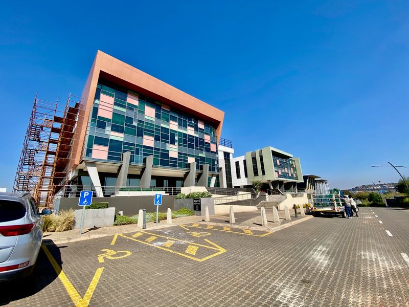 Modern commercial office building exterior featuring a glass facade, paved parking area, and ongoing maintenance scaffolding.