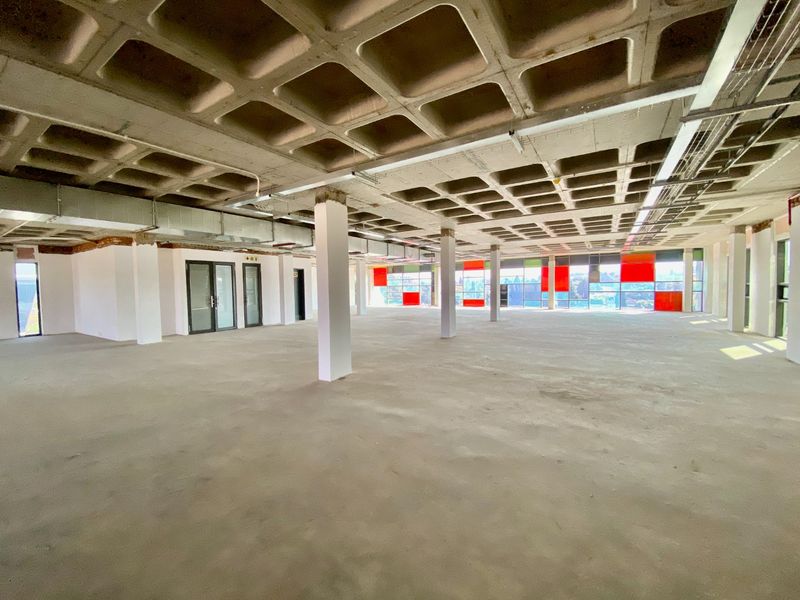 Expansive open-plan commercial office space featuring a raw waffle slab ceiling, exposed ducting, and large windows providing ample natural light.