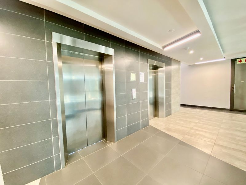 Modern commercial hallway featuring dual stainless steel elevator access, contemporary tiled wall finishes, and recessed ceiling lighting in a well-maintained professional building.