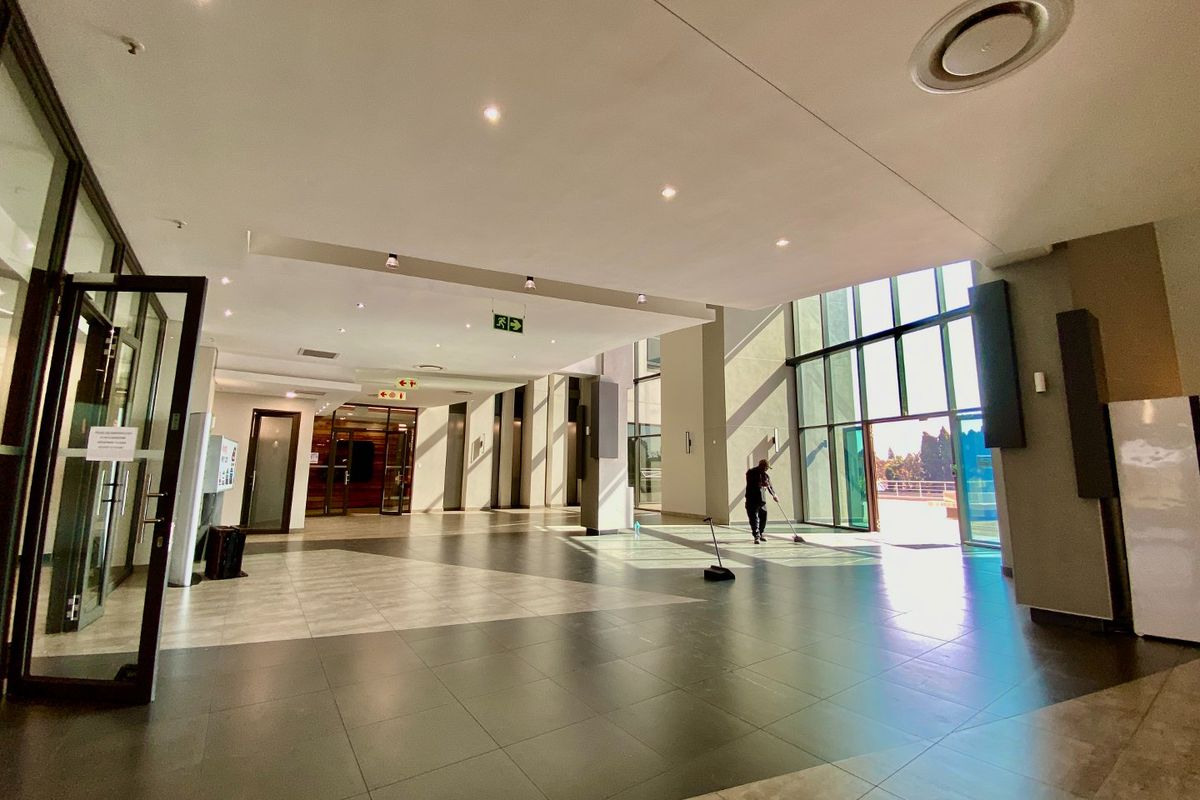 Spacious commercial entrance lobby featuring large format floor tiles, recessed lighting, and expansive floor-to-ceiling glass windows providing abundant natural light.