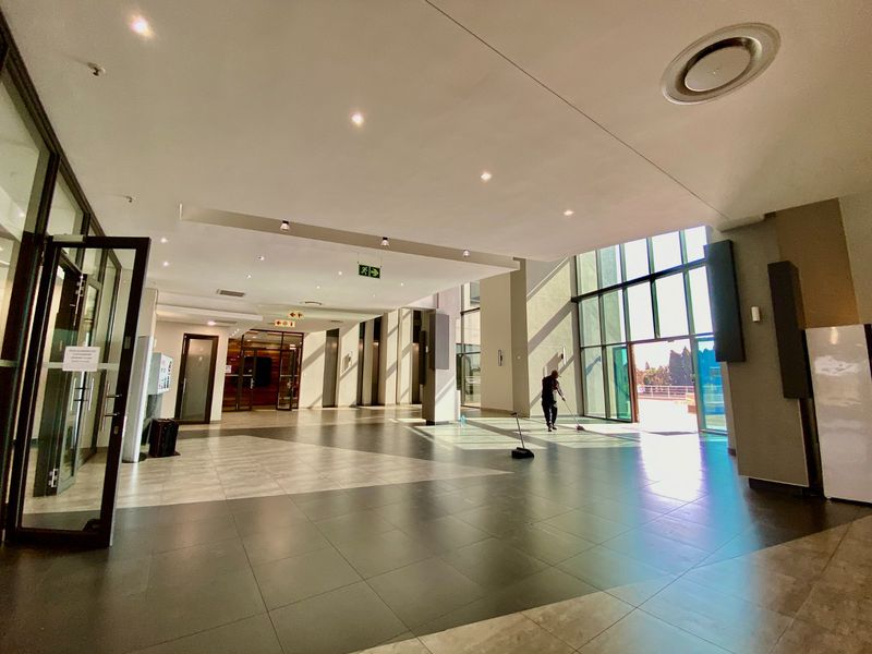 Spacious commercial entrance lobby featuring large format floor tiles, recessed lighting, and expansive floor-to-ceiling glass windows providing abundant natural light.