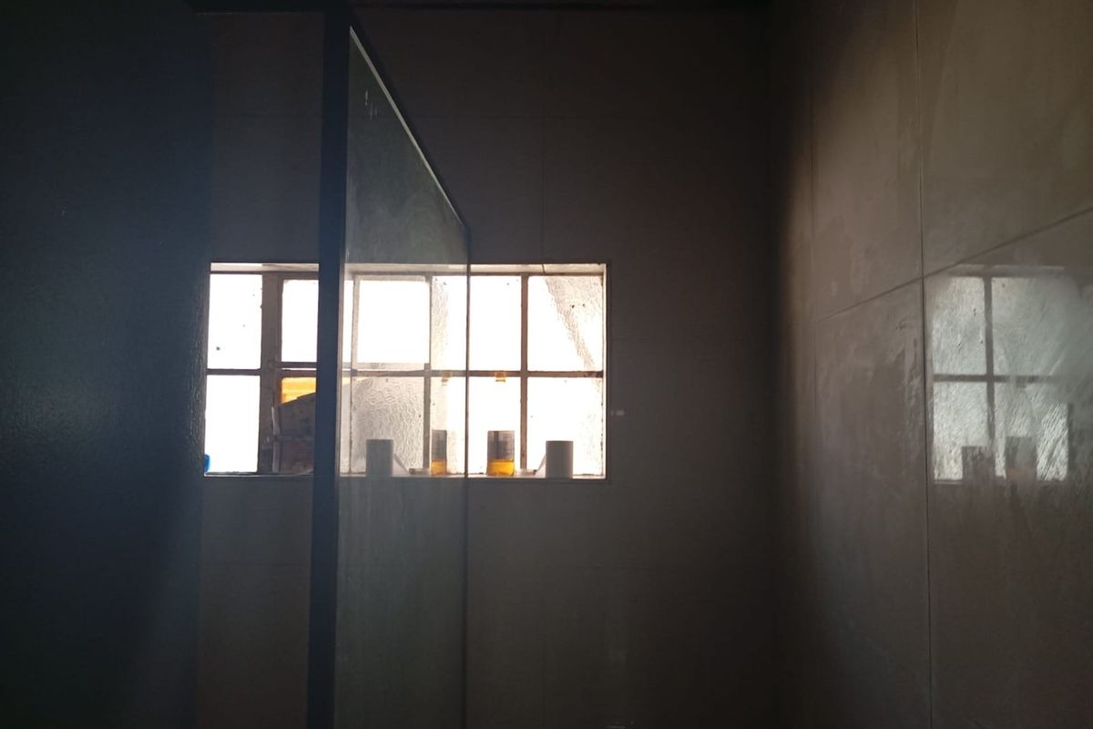 A dimly lit bathroom featuring tiled walls, a glass shower enclosure, and a toilet, requiring improved lighting to showcase the space effectively.