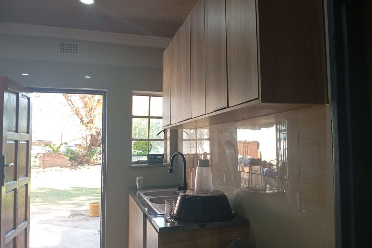 A functional kitchen area featuring modern wood-finish cabinetry, a tiled backsplash, and a sink, with direct access to the outdoor garden area.