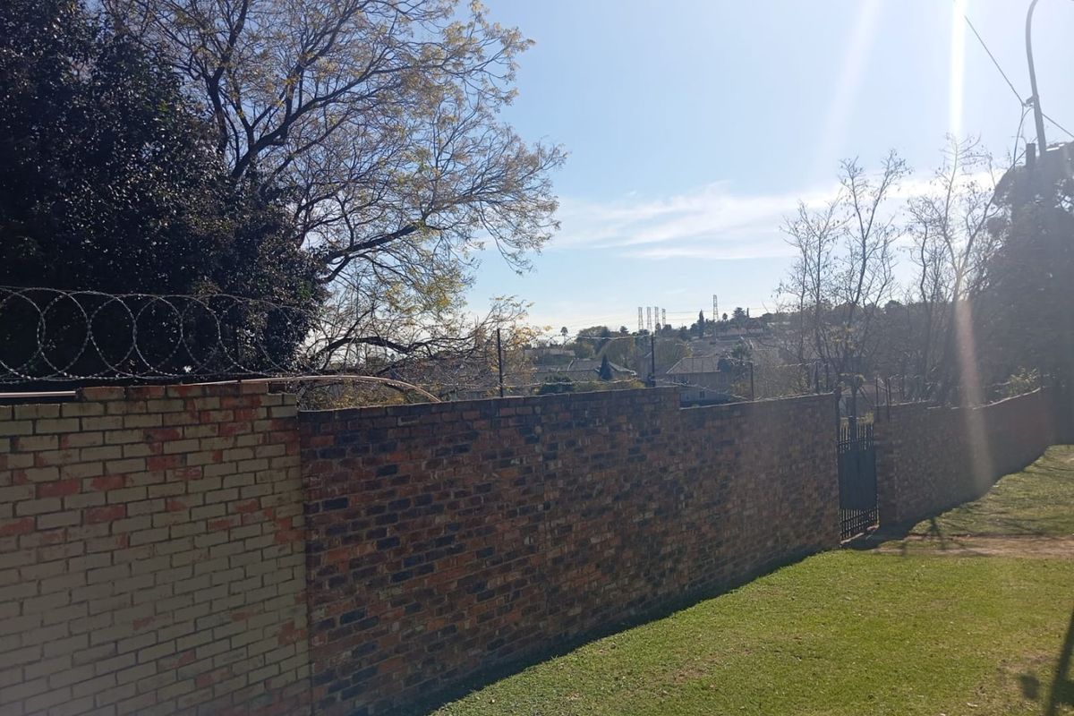 A view of the property's rear boundary featuring a brick wall topped with razor wire, a metal gate, and a maintained lawn area.
