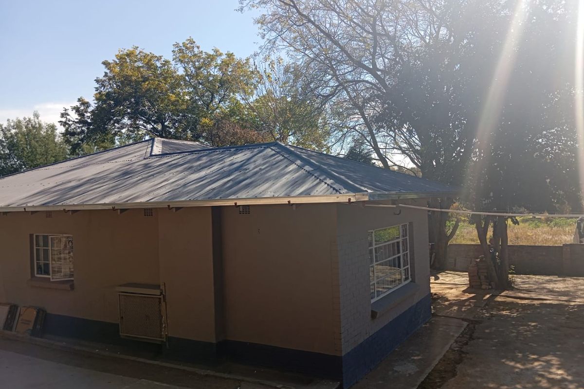 Rear view of the property showing the corrugated metal roof, brick exterior walls, and steel window frames set within a garden area.