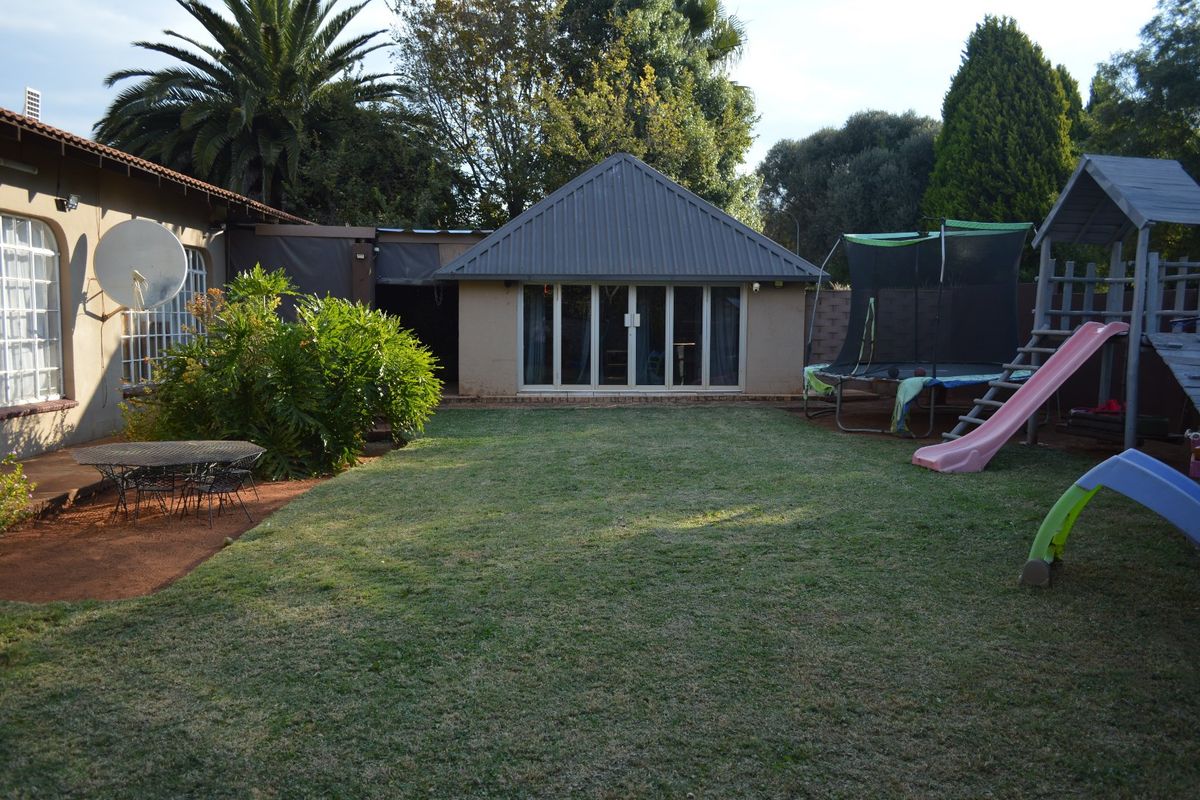 A spacious rear garden featuring a lawn area and a detached structure with a metal roof and sliding glass doors.