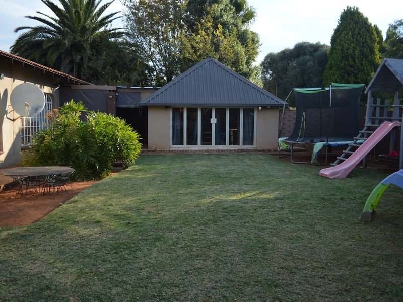 A spacious rear garden featuring a lawn area and a detached structure with a metal roof and sliding glass doors.