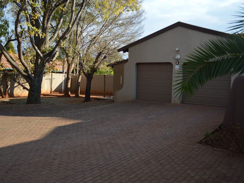 A view of the property's front exterior featuring a double garage, paved driveway, and established trees within a walled garden setting.