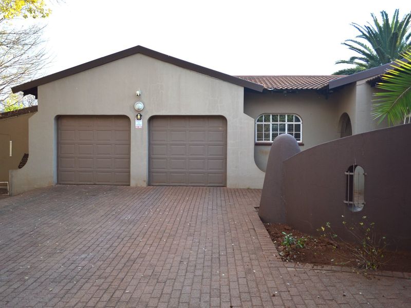 Front elevation of the property featuring a double garage, paved driveway, and a secure boundary wall with integrated lighting.