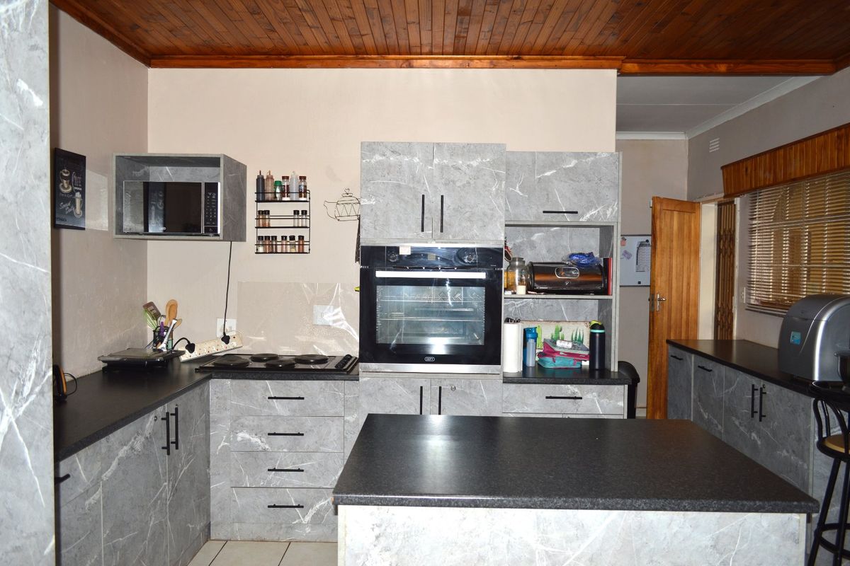 A functional kitchen featuring grey marble-effect cabinetry, built-in oven and hob, dark countertops, and a distinctive timber-paneled ceiling.