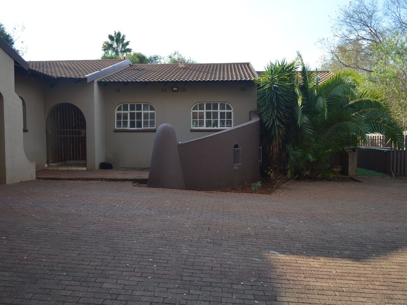 Front elevation of the property featuring a paved driveway, arched entrance gate, and traditional tiled roof architecture.