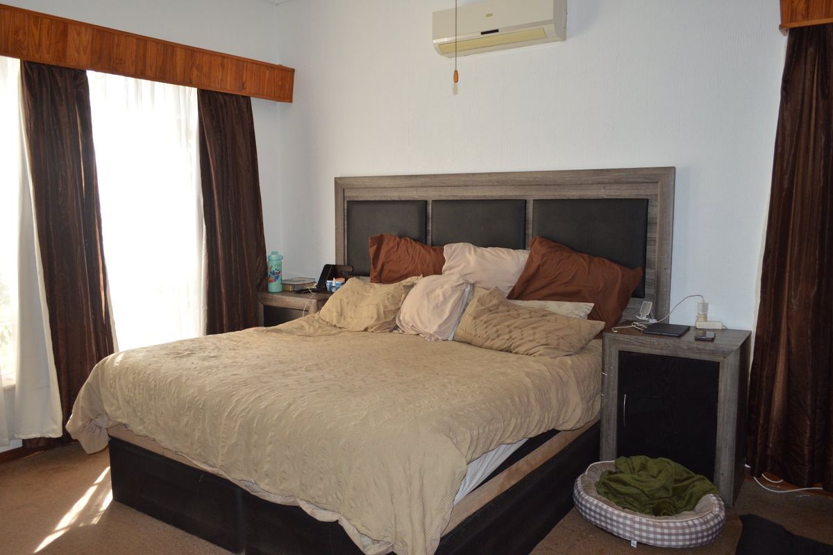 A bedroom featuring a wall-mounted air conditioning unit and a wooden curtain pelmet above the window.