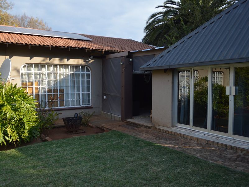 Rear view of the property featuring a combination of tiled and metal roofing, solar panels, and paved patio area leading to the garden.