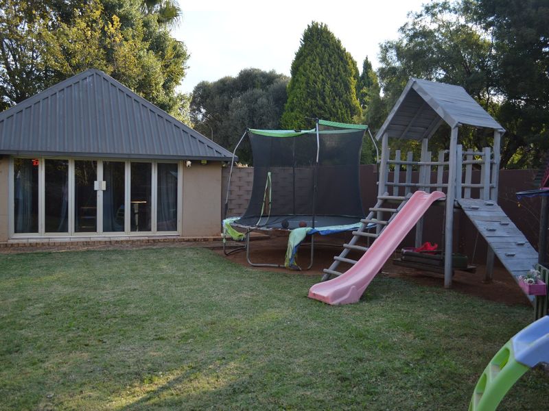 Rear garden view featuring a lawn area, brick boundary wall, and a detached structure with a metal roof and sliding glass doors.