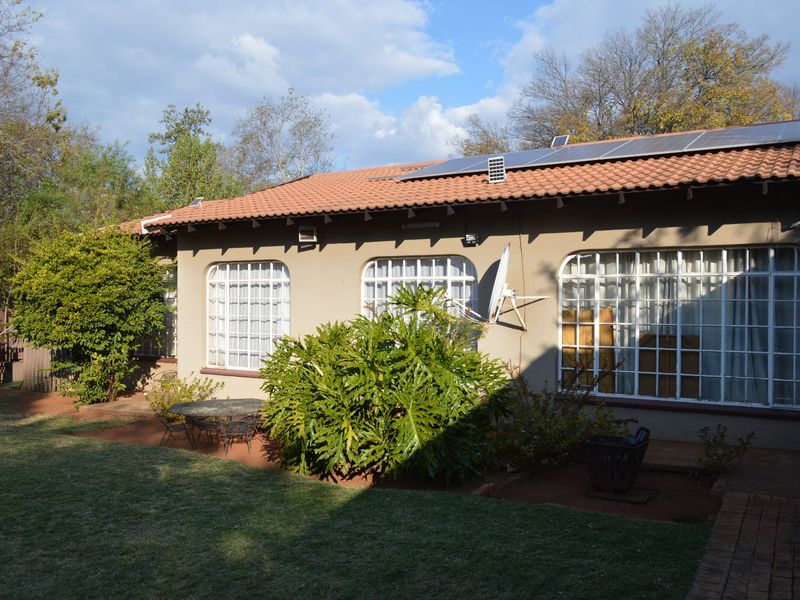Rear view of the house featuring a terracotta tiled roof with solar panels, security-barred windows, and a paved patio area overlooking the garden.