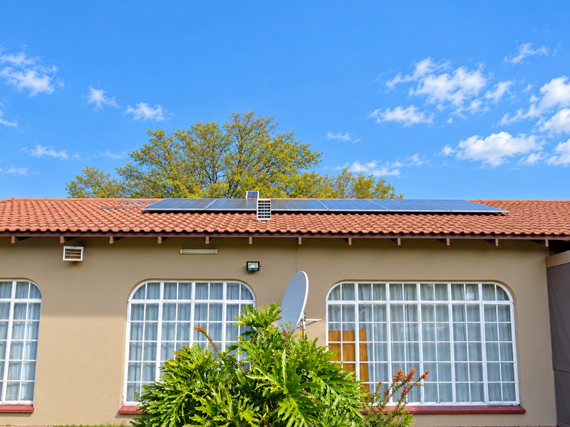 Rear exterior view of the house featuring terracotta roof tiles, installed solar panels, and arched windows with white frames.