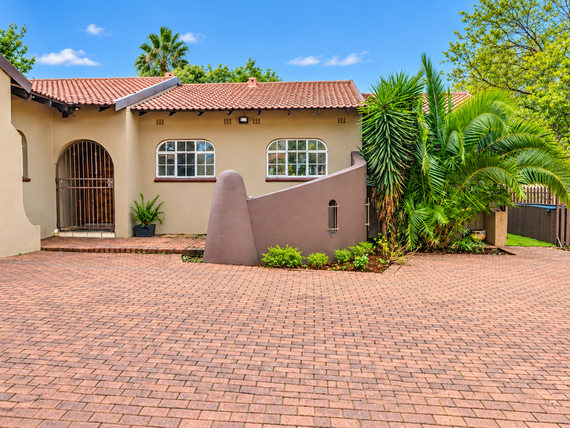 Front elevation of a well-maintained house featuring a brick-paved driveway, terracotta roof tiles, and a secure arched entrance with established garden landscaping.