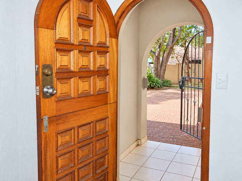 Entrance area featuring a classic arched timber door, tiled flooring, and a wrought iron security gate leading to a brick-paved outdoor space.