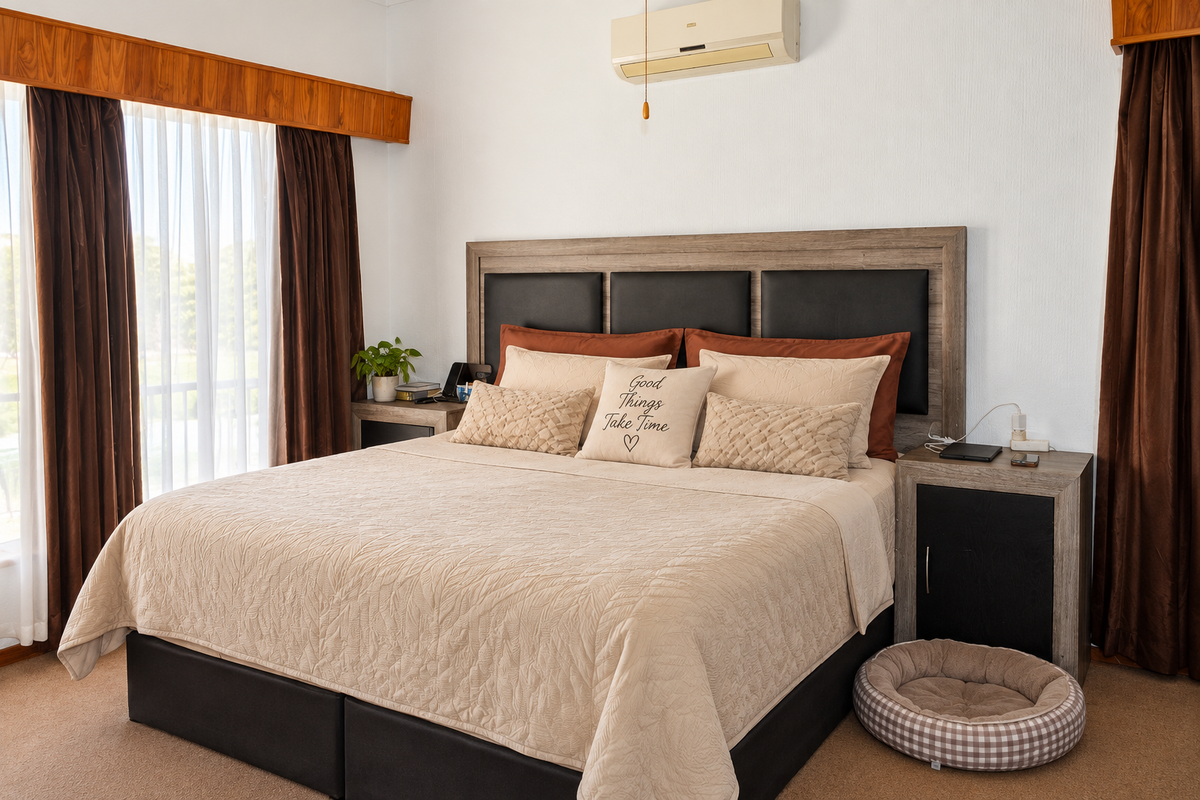 A well-maintained bedroom featuring carpeted flooring, a wall-mounted air conditioning unit, and timber pelmets above the window treatments.