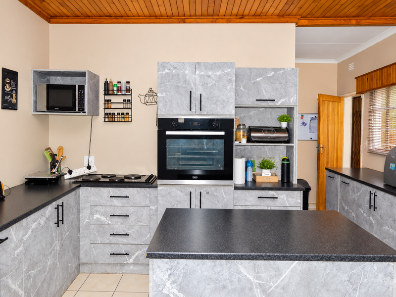 A modern kitchen featuring grey marble-effect cabinetry, a built-in oven and hob, dark countertops, and a warm timber-paneled ceiling.