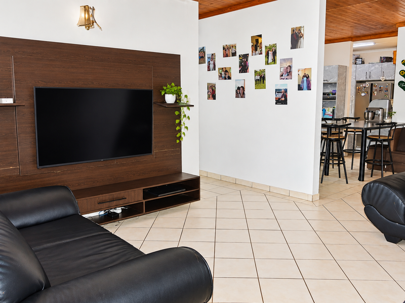 Open-plan living area featuring tiled flooring, a timber-paneled ceiling, and a built-in dark wood media unit, flowing into the adjacent kitchen space.