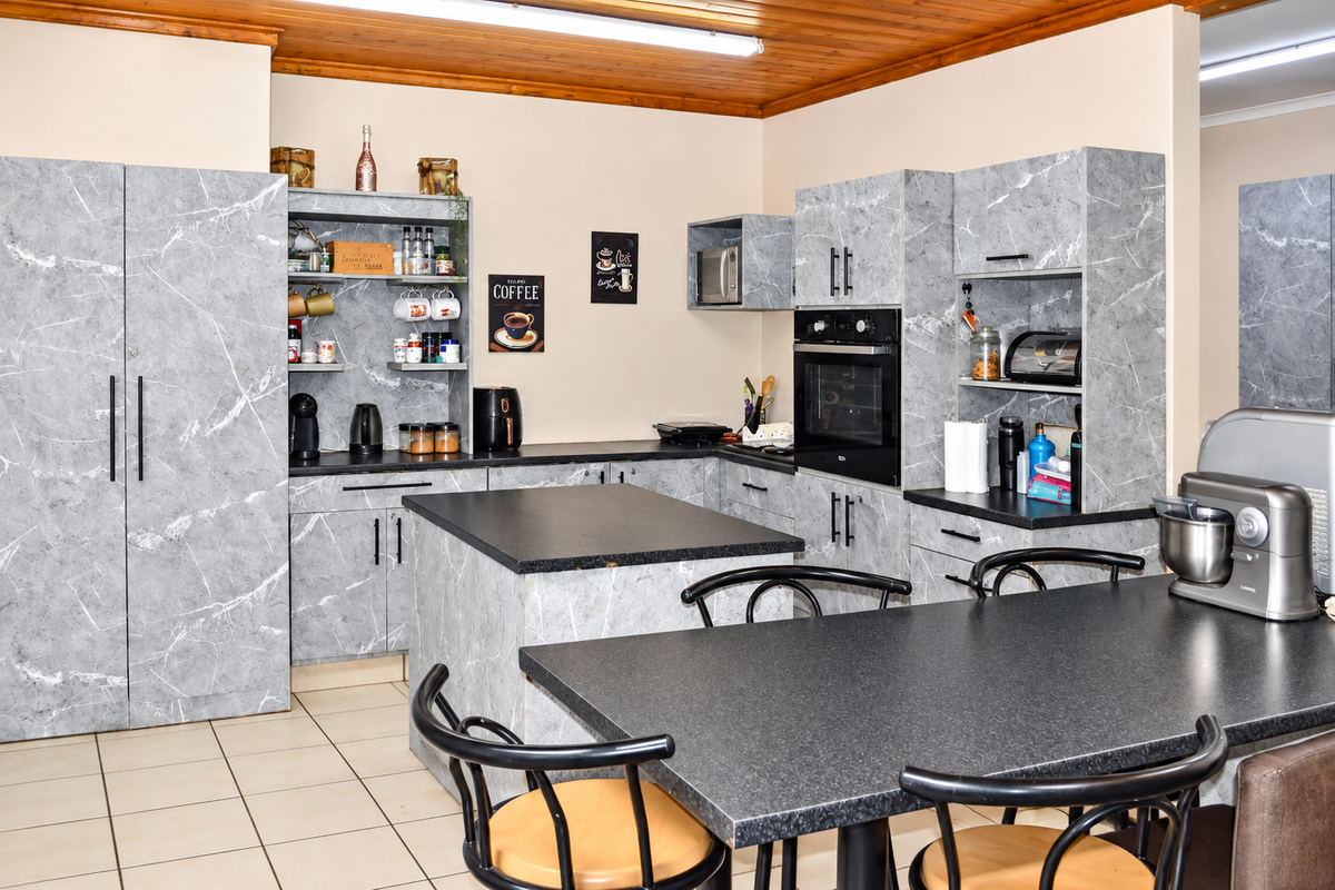 A functional kitchen featuring marble-effect cabinetry, a central island, built-in oven and microwave, and a warm timber ceiling finish.