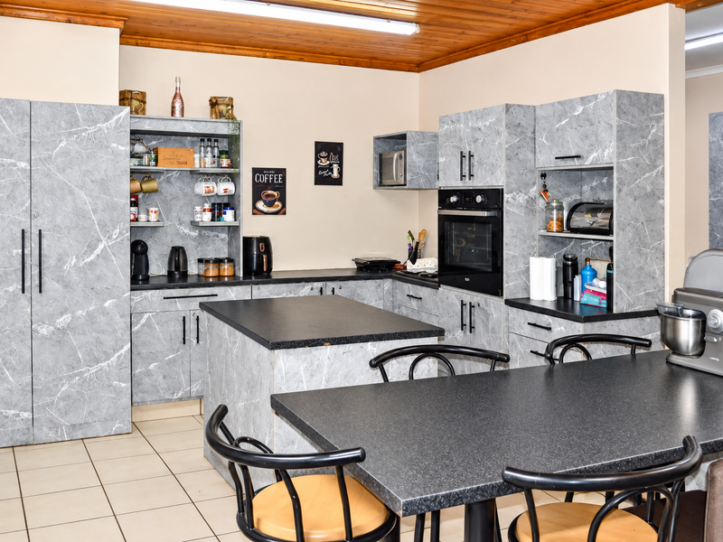 A functional kitchen featuring marble-effect cabinetry, a central island, built-in oven and microwave, and a warm timber ceiling finish.