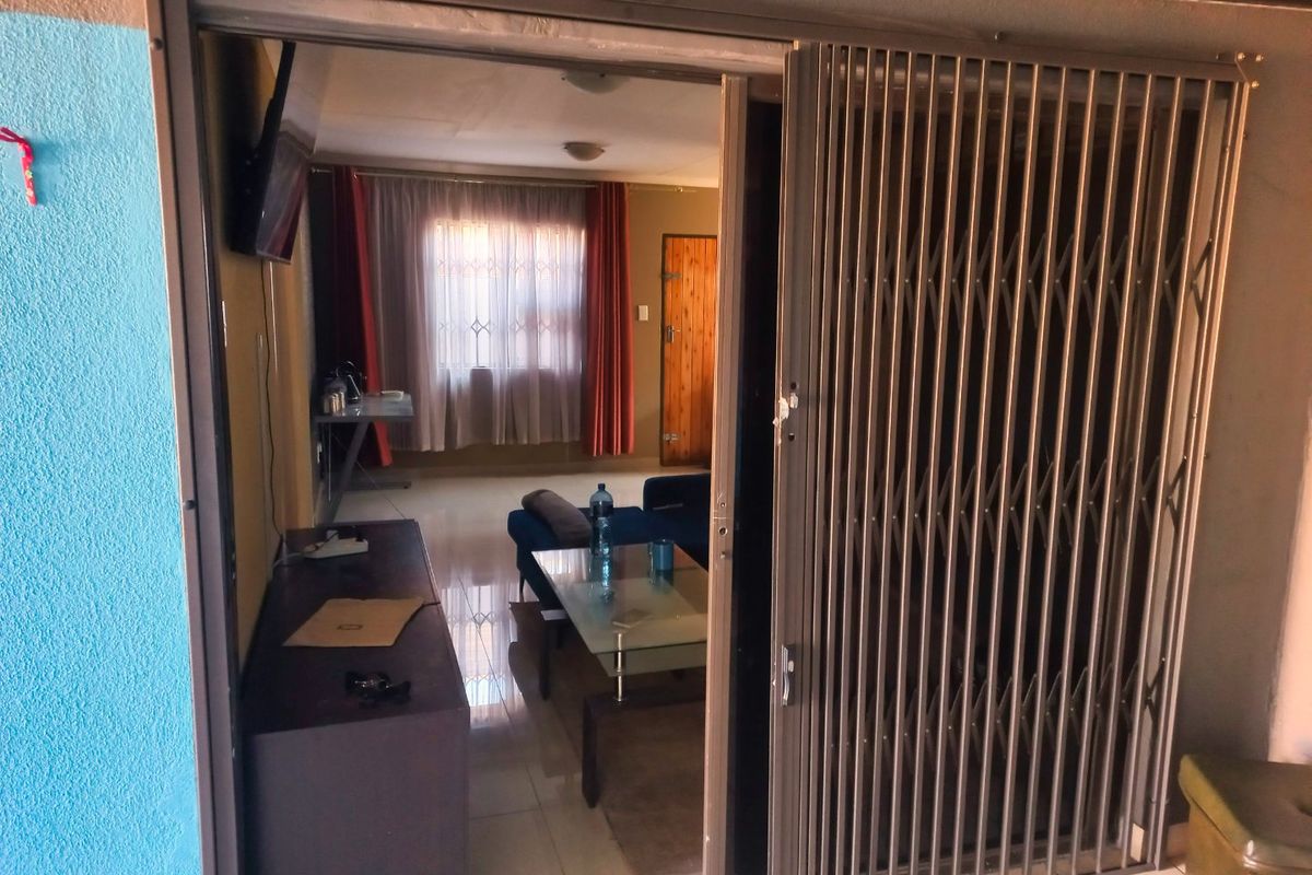 A living room area viewed through a sliding security gate, featuring tiled flooring and natural light from a window.