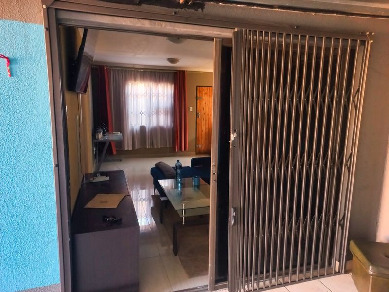 A living room area viewed through a sliding security gate, featuring tiled flooring and natural light from a window.